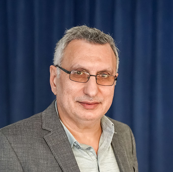 Person mit Brille und grauem Sakko vor blauem Vorhang