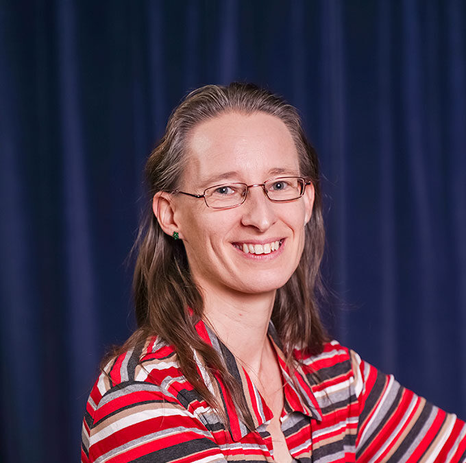 Person mit Brille und gestreiftem Oberteil vor blauem Vorhang