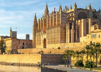 Große gotische Kathedrale aus Sandstein am Wasser mit Palmen und Stadtmauer im Vordergrund