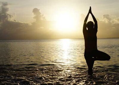 Silhouette einer Person in Baumhaltung im flachen Meer vor Sonnenuntergang und Wolkenhorizont