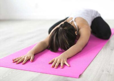 Person in Yogaposition mit ausgestreckten Armen auf pinker Yogamatte am Boden