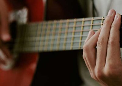 Hände greifen Akkord auf roter Akustikgitarre, Nahaufnahme von Griffbrett und Saiten