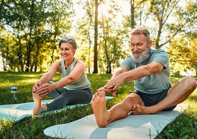 Zwei ältere Personen sitzen auf Yogamatten im Park und dehnen Beine im Sitzen