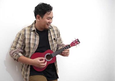 Person mit kariertem Hemd spielt rote Ukulele vor weißer Wand