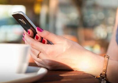 Hände mit rotem Nagellack halten Smartphone über Holztisch, unscharfe Kaffeetasse im Vordergrund